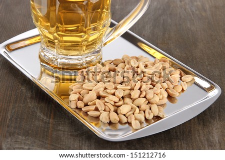 Beer in glass and nuts on tray on wooden table