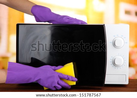 Hand with sponge cleaning  microwave oven, on bright background