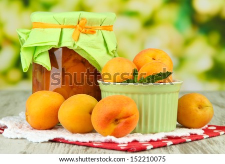 Apricot jam in glass jar and fresh apricots, on wooden table, on bright background
