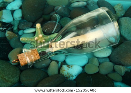 Bottle with letter on sea bottom with shells and stones