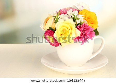 Beautiful bouquet of bright flowers in color mug, on wooden table, on  light background