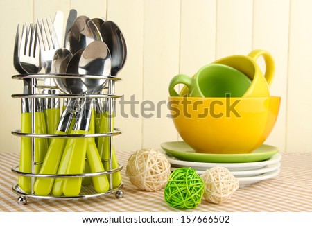 Kitchen cutlery in metal stand with clean dishes on tablecloth on beige background
