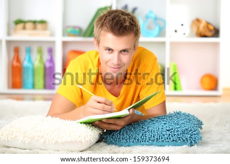 Young man lies on carpet and studying, on home interior background