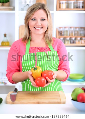 Happy smiling woman in kitchen  holding fresh vegetables in her hands