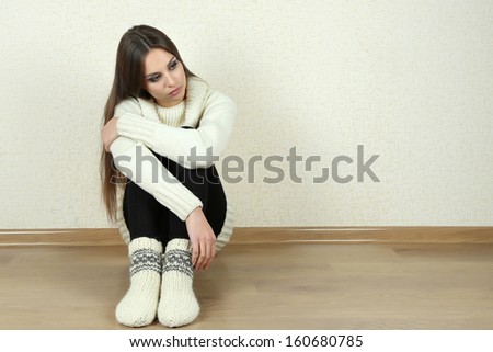 Sad woman sitting on floor near wall
