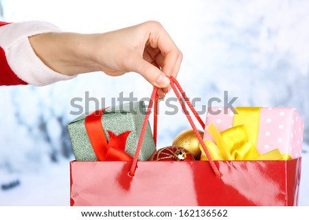 Hand holds package with New Year balls and gifts on snow background