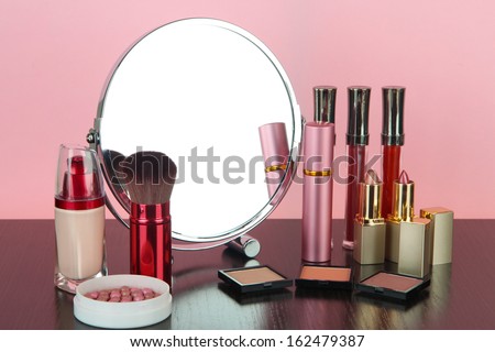 Round table mirror with cosmetics on table on pink background