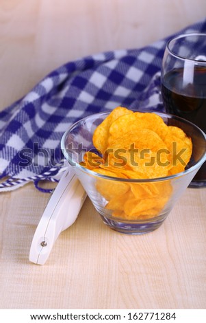 Chips in bowl, cola and TV remote on wooden table close-up