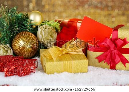 Gift boxes with blank label and Christmas decorations on snow on bright background