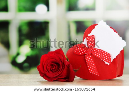 Gift box with blank label and rose on table on bright background