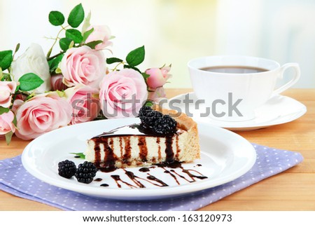 Slice of cheesecake with chocolate sauce and blackberry on plate, on wooden  table, on bright background