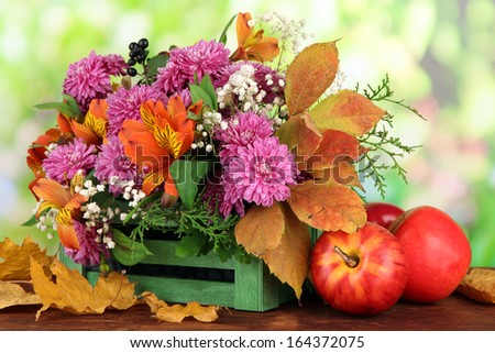 Flowers composition in crate with apples on table on bright background