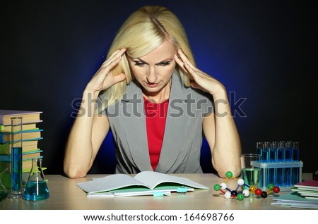 Tired chemistry teacher sitting at table on dark colorful background