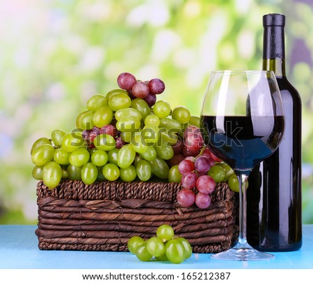 Ripe green and purple grapes in basket with wine on wooden table on natural background