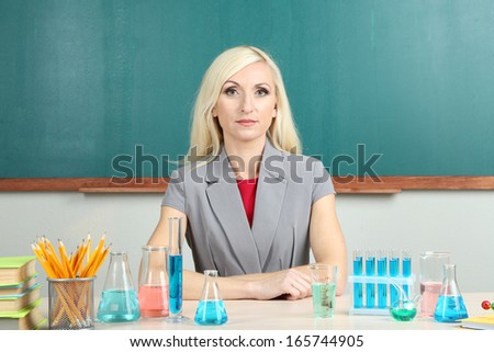 Chemistry teacher sitting at table on blackboard background