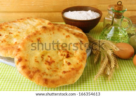Pita breads on wooden stand with spices and spikes on tablecloth on wooden background