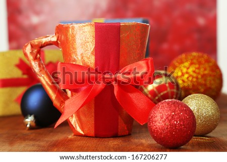 Cup packed in gift paper with gifts on wooden table on bright background