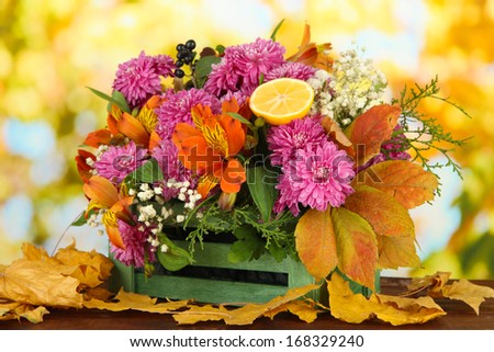 Flowers composition in crate with yellow leaves on table on bright background