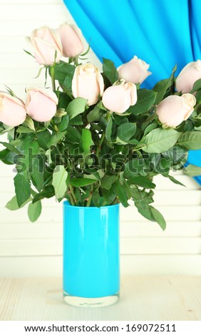 Beautiful bouquet of roses in vase, on light wooden background