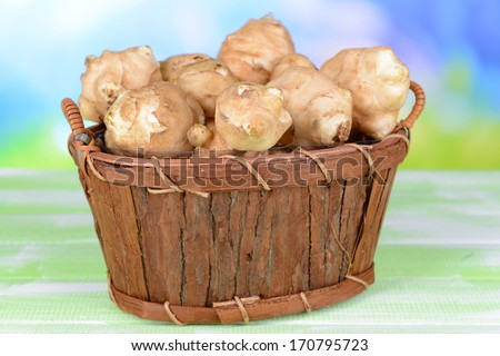 Topinambur roots in wooden basket on table on light background