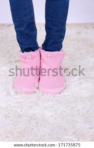 Female legs in blue jeans trousers and home winter shoes, on white carpet background