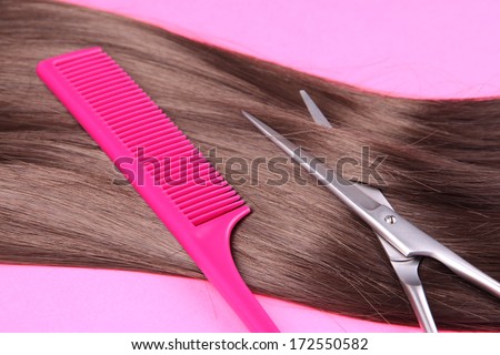 Long brown hair with comb and scissors on pink background