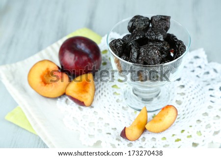 Fresh and dried plums in glass bowl on napkin, on wooden background