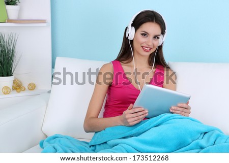 Beautiful young woman listening music on sofa on blue background
