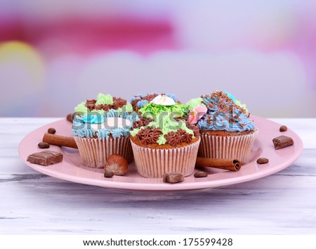Tasty cupcakes with butter cream, on plate, on color wooden table, on light background