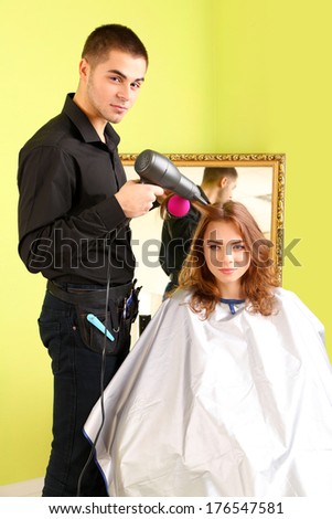 Young man hairdresser makes hairstyle girl in beauty salon