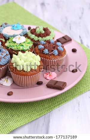 Tasty cupcakes with butter cream, on plate, on color napkin, on color wooden background