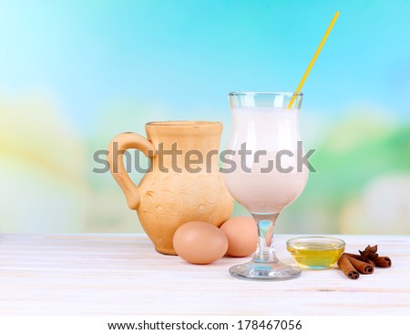 Eggnog with milk and eggs on wooden table and natural background