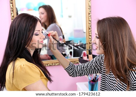 Young woman stylist doing makeup beautiful girl in beauty salon