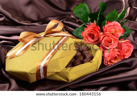 Delicious chocolates in box with flowers on brown background