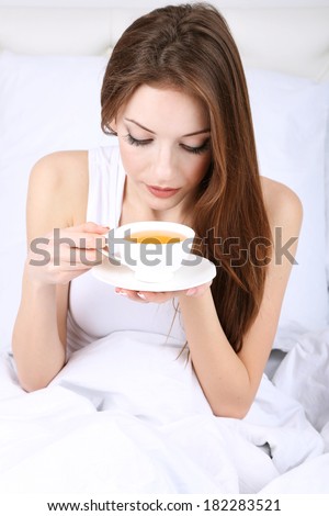Young beautiful woman with cup of tea in bed close-up