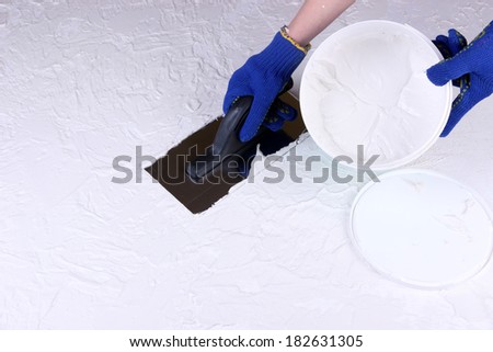 Construction trowel and worker hands on wall with textured plaster