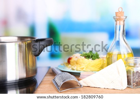 Process of preparing pasta. Composition with row spaghetti in pan, grater, cheese, on wooden table  on bright background