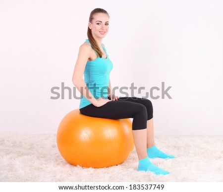 Young beautiful fitness girl exercising with orange ball in gym
