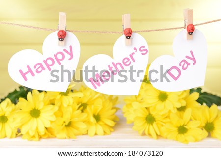 Happy Mothers Day message written on paper hearts with flowers on yellow background