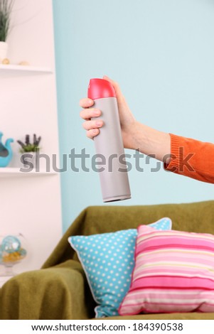 Sprayed air freshener in hand on home interior background