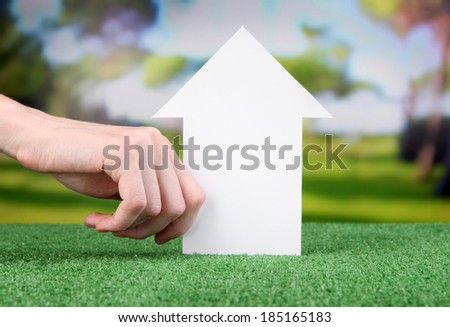 Little paper house in hand close-up, on green grass, on bright background