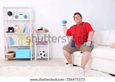 Large fitness man making exercises with dumbbells, at home