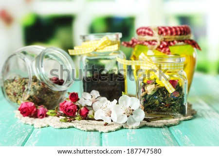 Assortment of herbs, honey and tea in glass jars on wooden table, on bright background
