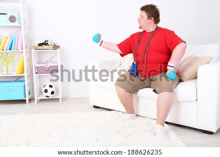 Large fitness man making exercises with dumbbells, at home
