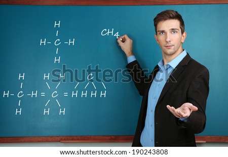 Young teacher writing chemical formula on blackboard