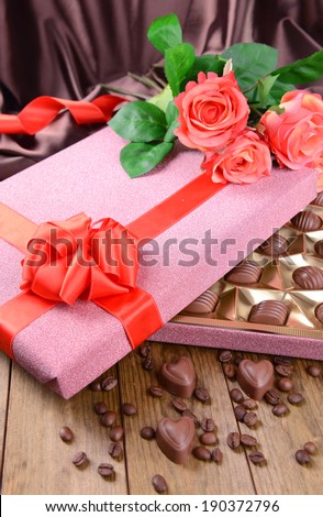 Delicious chocolates in box with flowers on table on brown background