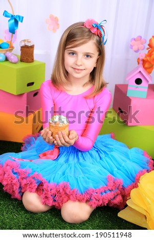 Beautiful small girl in petty skirt holding Easter cake on decorative background