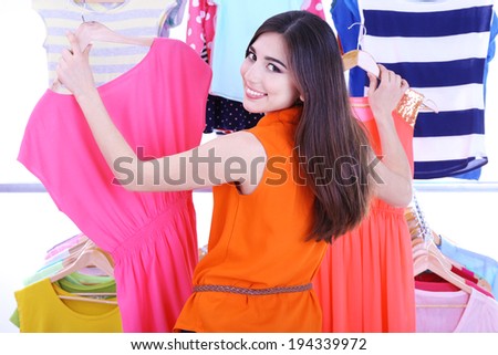 Young woman choose clothes near rack with hangers