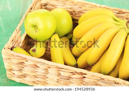 Bunch of mini bananas in wicker box on color wooden background