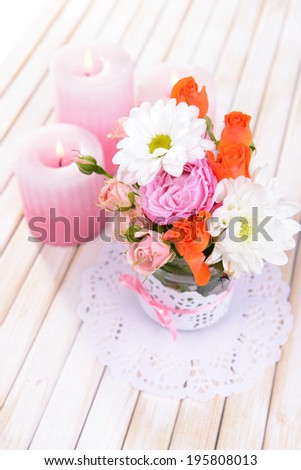 Beautiful bouquet of bright flowers in jar on table on light background